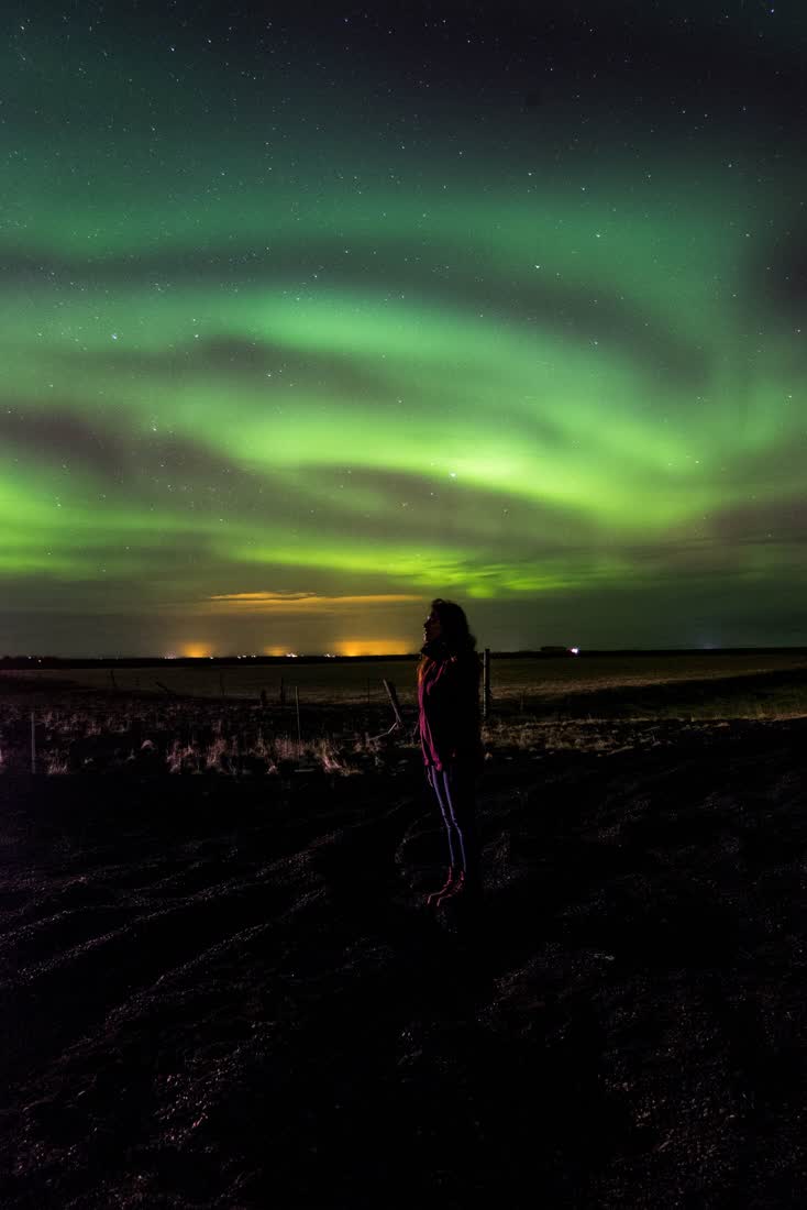 A figure standing under a green aurora over open country