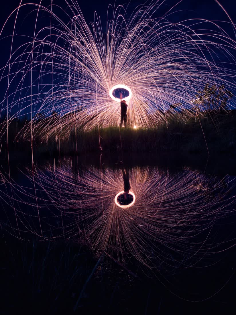Steel wool spun into a ring of sparks, mirrored in still water