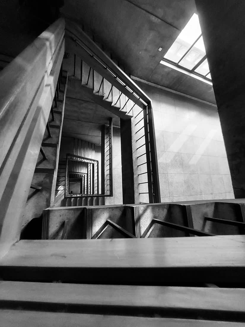 A concrete stairwell spiralling downward, in black and white